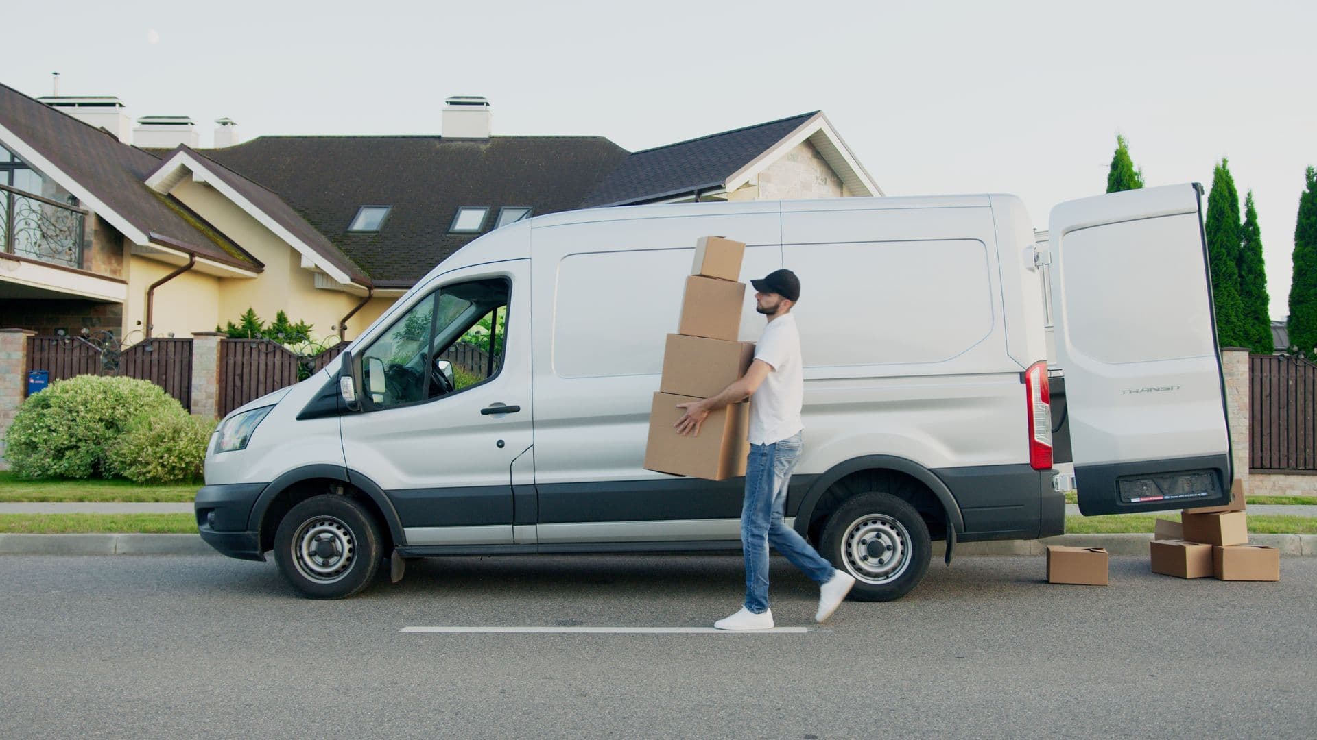 Courier carrying a stack of boxes beside a white delivery van on a sunny street